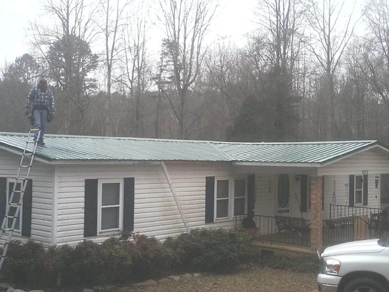 Worker on a ladder beside a new green metal roof on a ranch home in Camden Point