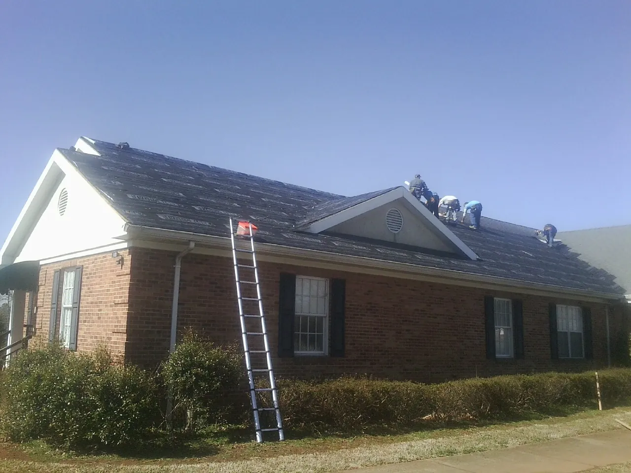 Crew tearing shingles off a brick ranch roof with a ladder set — Emergency Roof Repair work by our crew in Camden Point