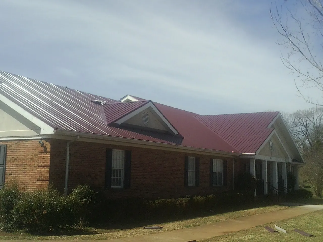 Red metal roof with gabled entries on a long brick building, from a Hail Damage Roof Repair job in Camden Point