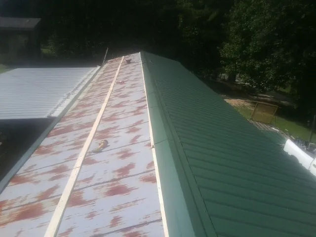 Old rusted panels beside newly installed green metal roofing — Wind Damage Roof Repair by Roofing Brothers in Camden Point