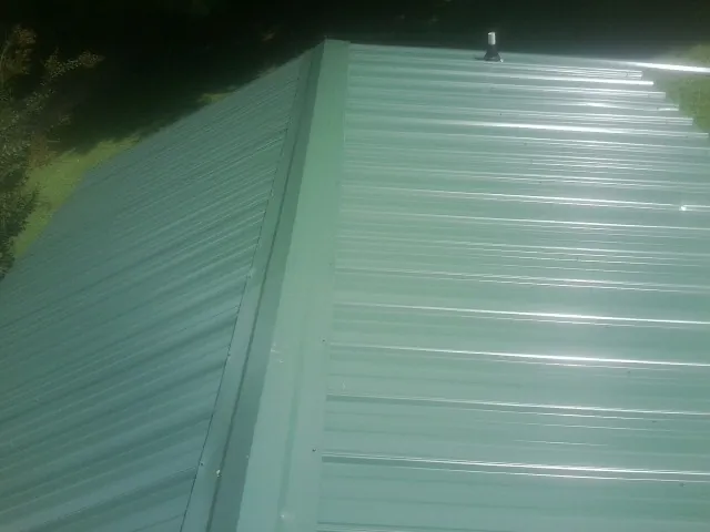 New green metal panels meeting at the ridge of a roof — Flat Roof Repair work by our crew in Camden Point