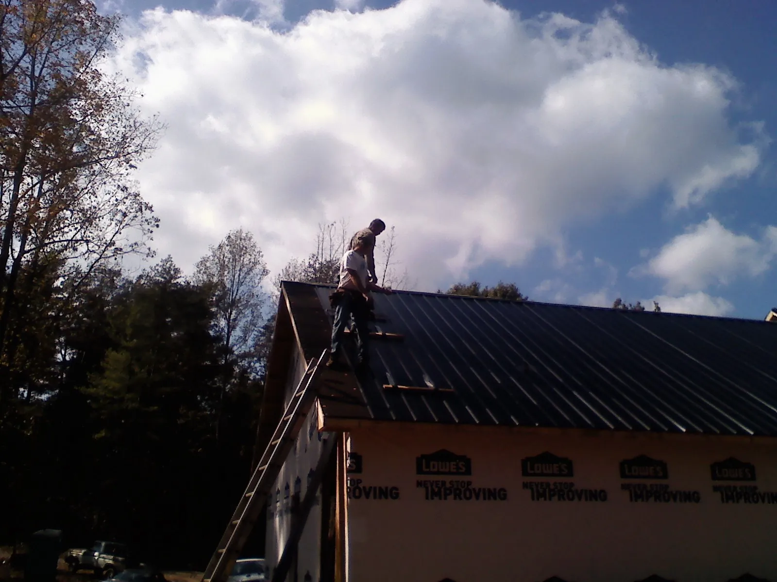 Roofer fastening dark metal panels high against a cloudy sky, from a Roof Inspection job in Camden Point