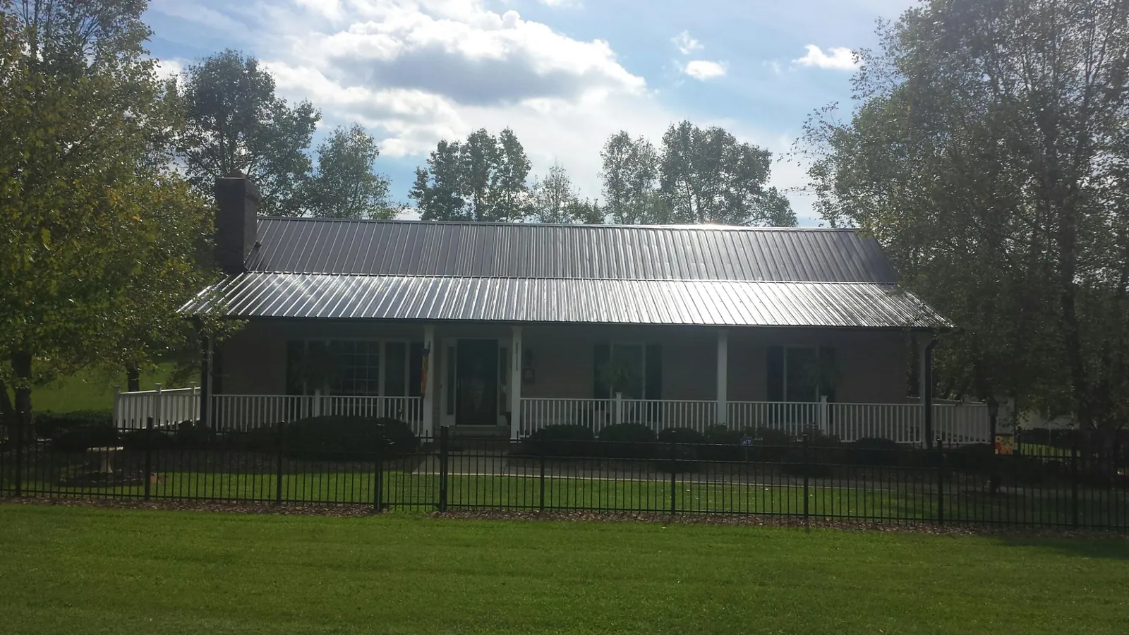 Gray metal roof on a brick ranch with a full width front porch — Gutter Guard Installation work by our crew in Camden Point