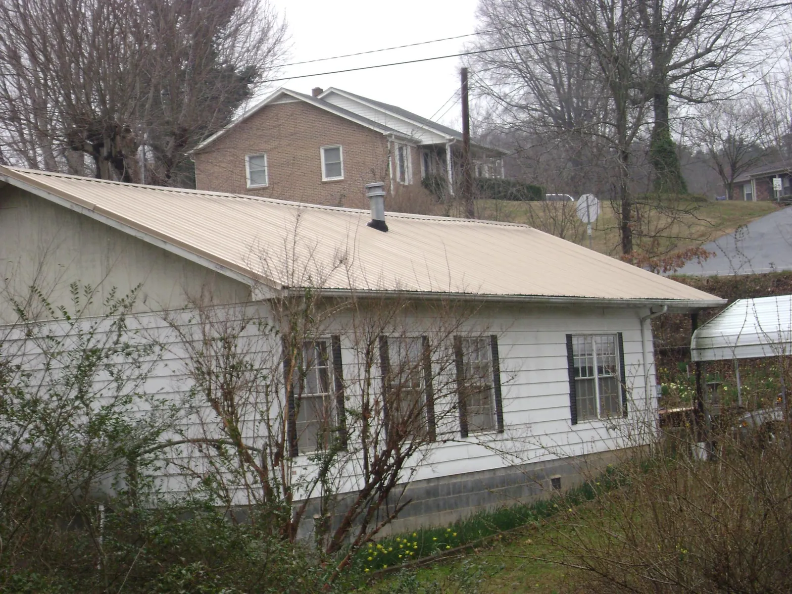 Tan metal roof on a white sided house set into a hillside — Commercial Roofing by Roofing Brothers in Camden Point